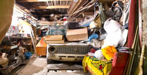 Garage inside. Old broken car, shelves with tools and stacks of things.